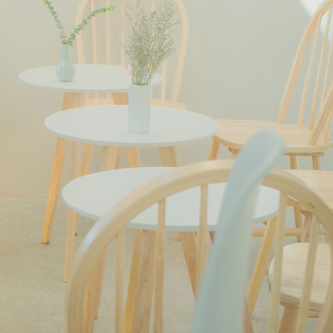 Light wooden chairs and tables with white cushions in a softly lit room.