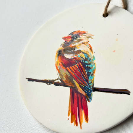 Round ceramic ornament with a colorful bird design on a white background